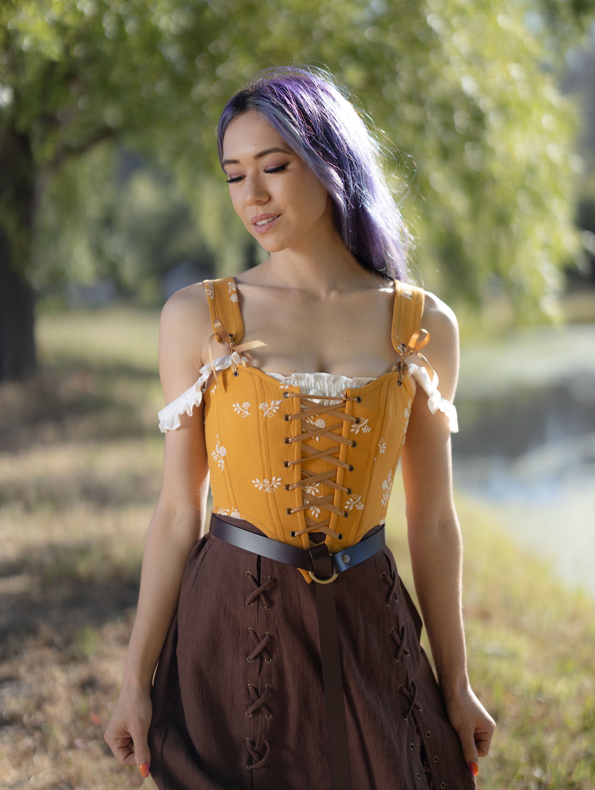 Woman outdoors wearing a mustard yellow Renaissance corset with front lacing and removable straps over a brown skirt