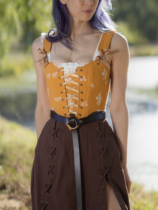 Person wearing a yellow corset with floral patterns outdoors.