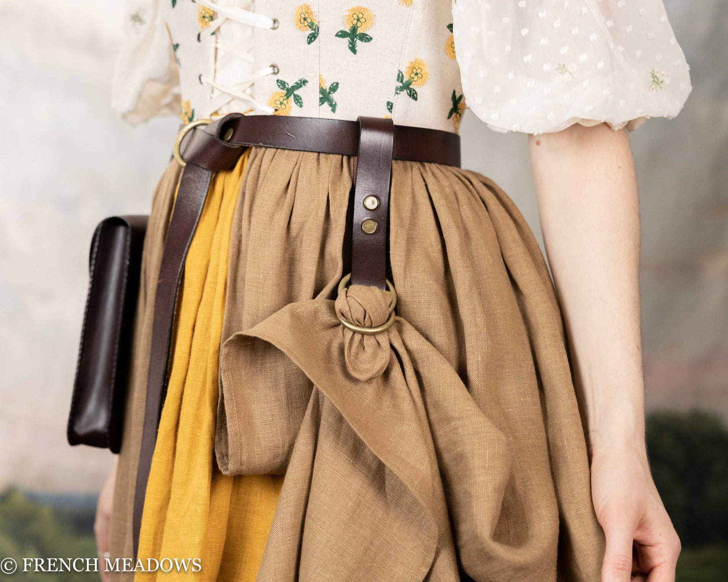 Leather skirt hike attached to brown belt lifting tan renaissance dress skirt, showing decorative gathering detail
