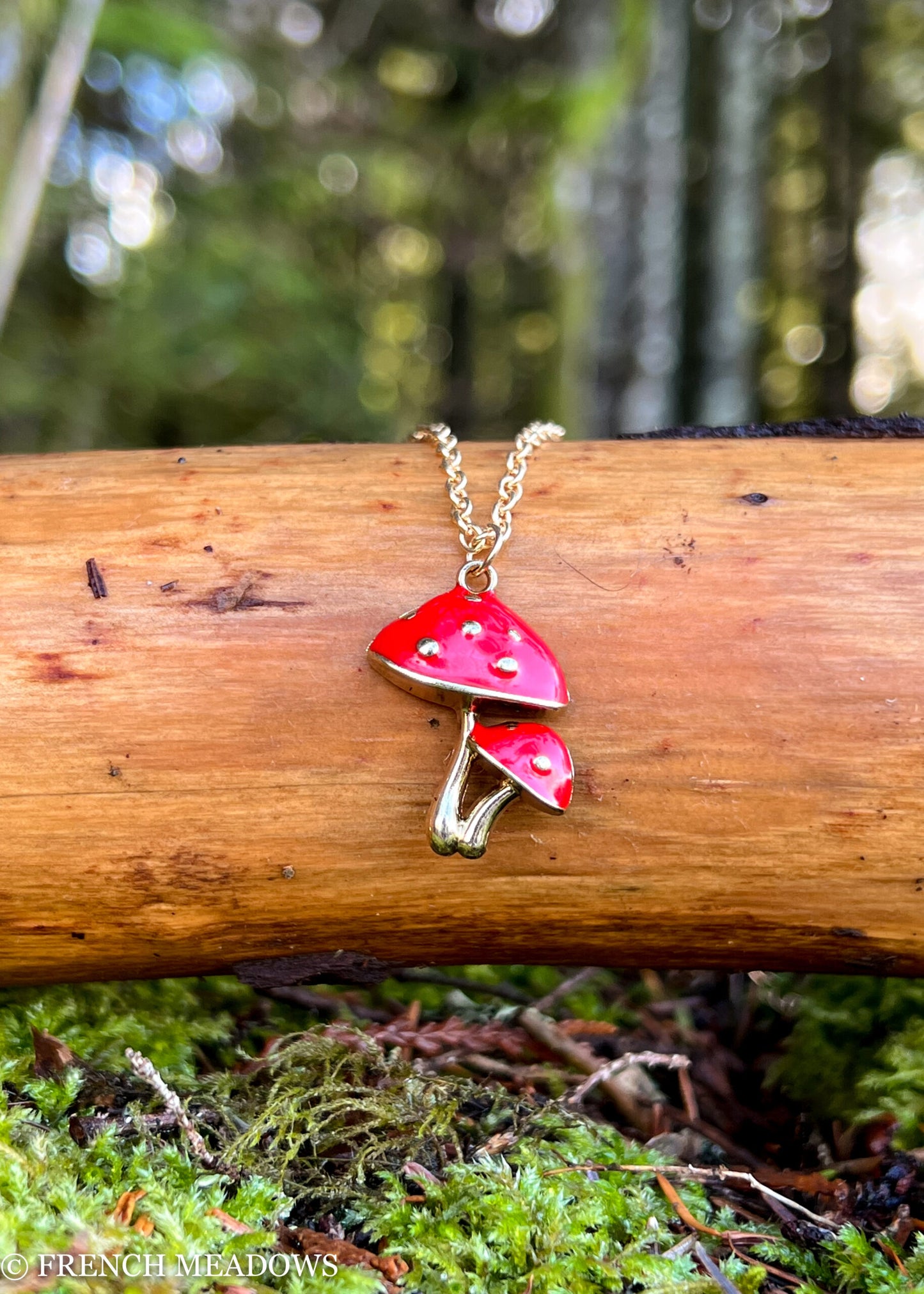 Amanita Mushroom Necklace featuring red and white spotted mushroom pendant on gold chain displayed on wooden log in forest setting