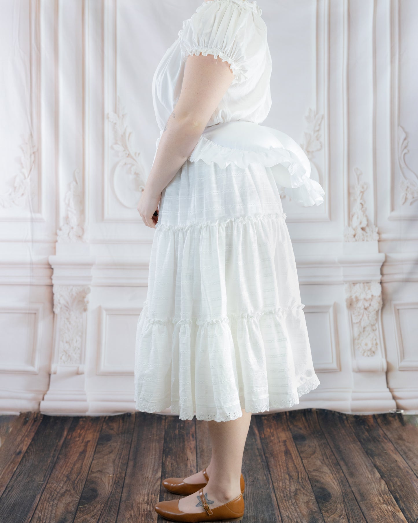 Woman wearing white dress with Bustle Pad underneath to add volume and shape to the skirt's back silhouette