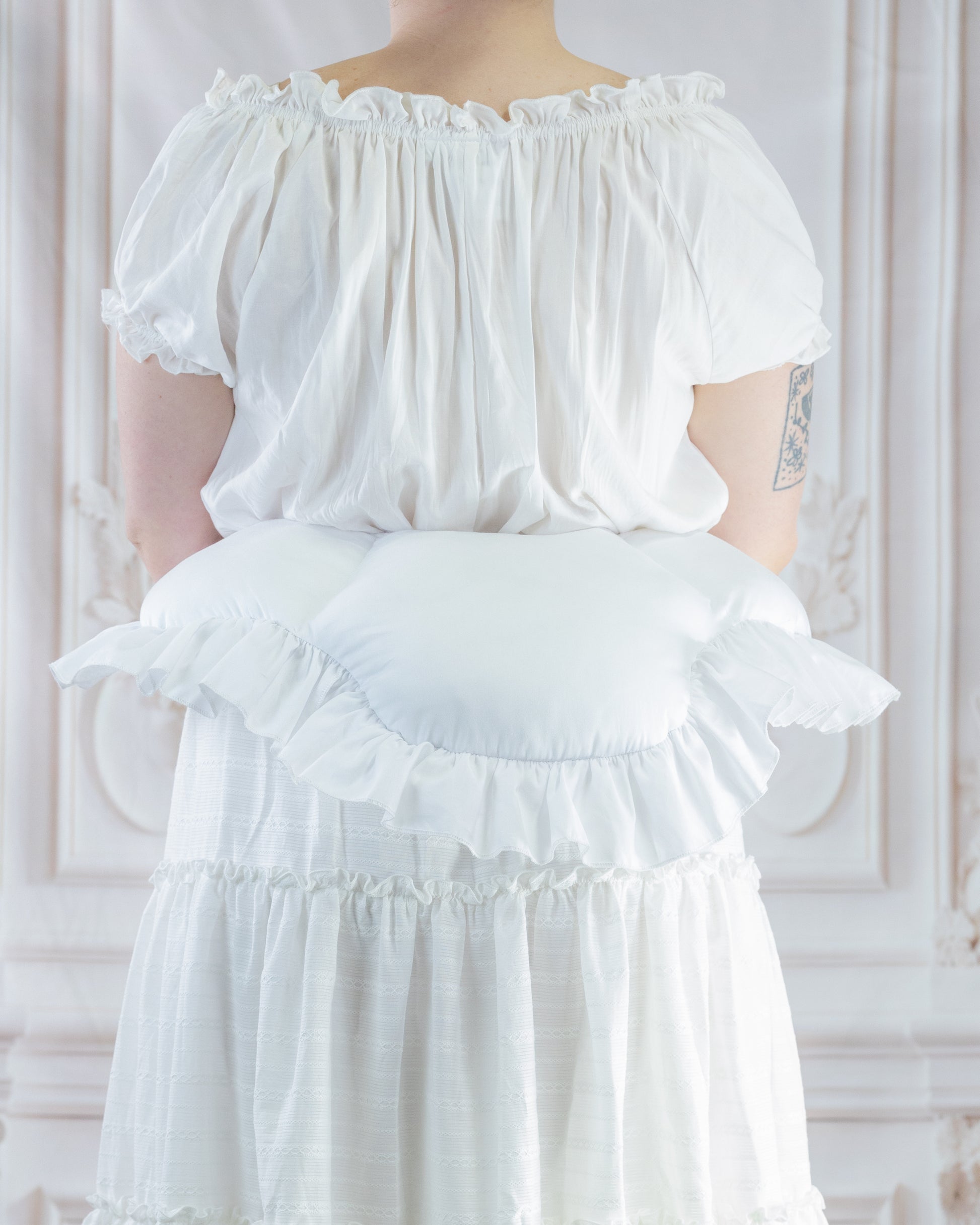 Woman wearing white dress with a ruffled 18th Century Bustle Pad creating a lifted silhouette from the back