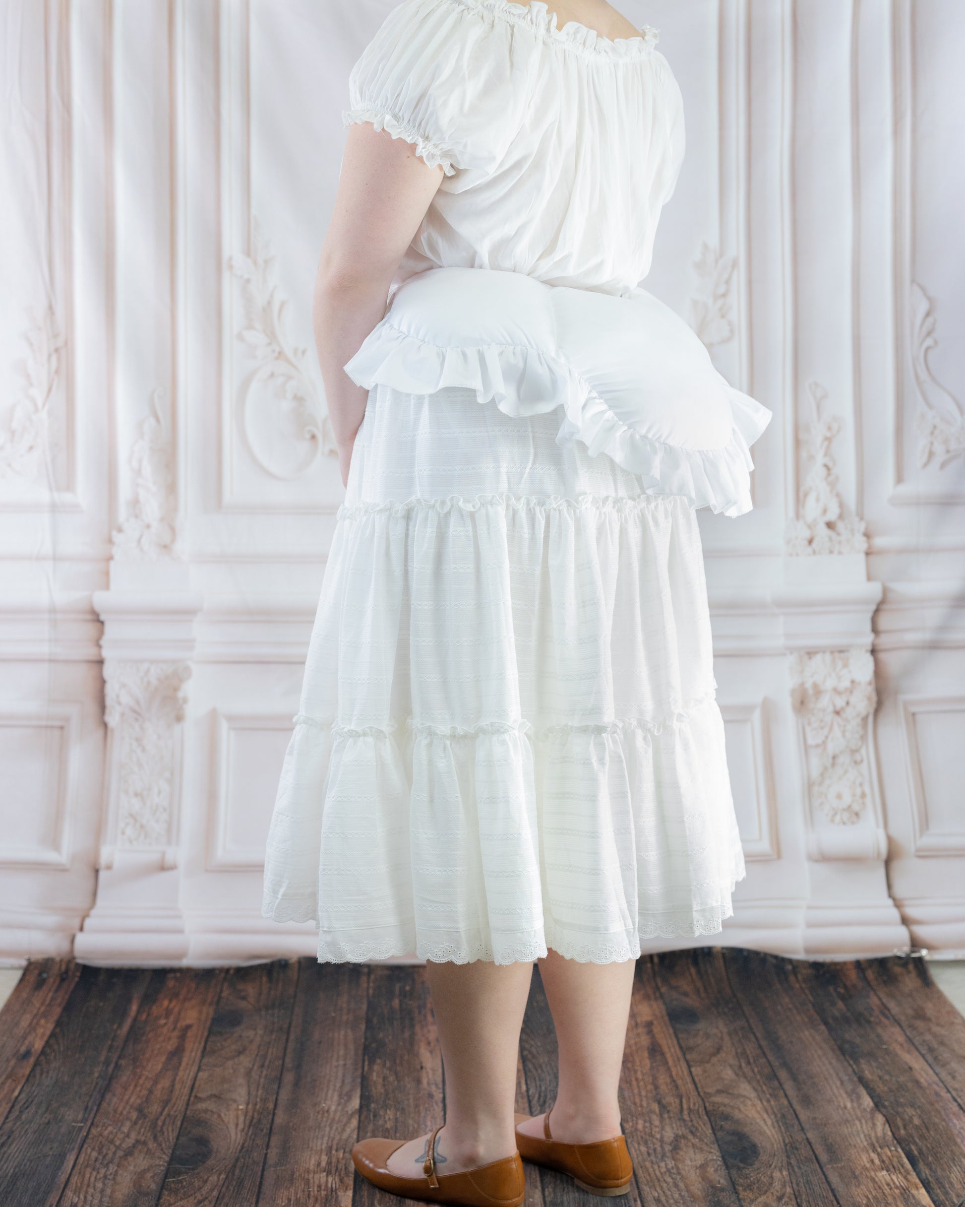 Woman wearing a white dress with an 18th Century Bustle Pad enhancing the skirt's back silhouette.
