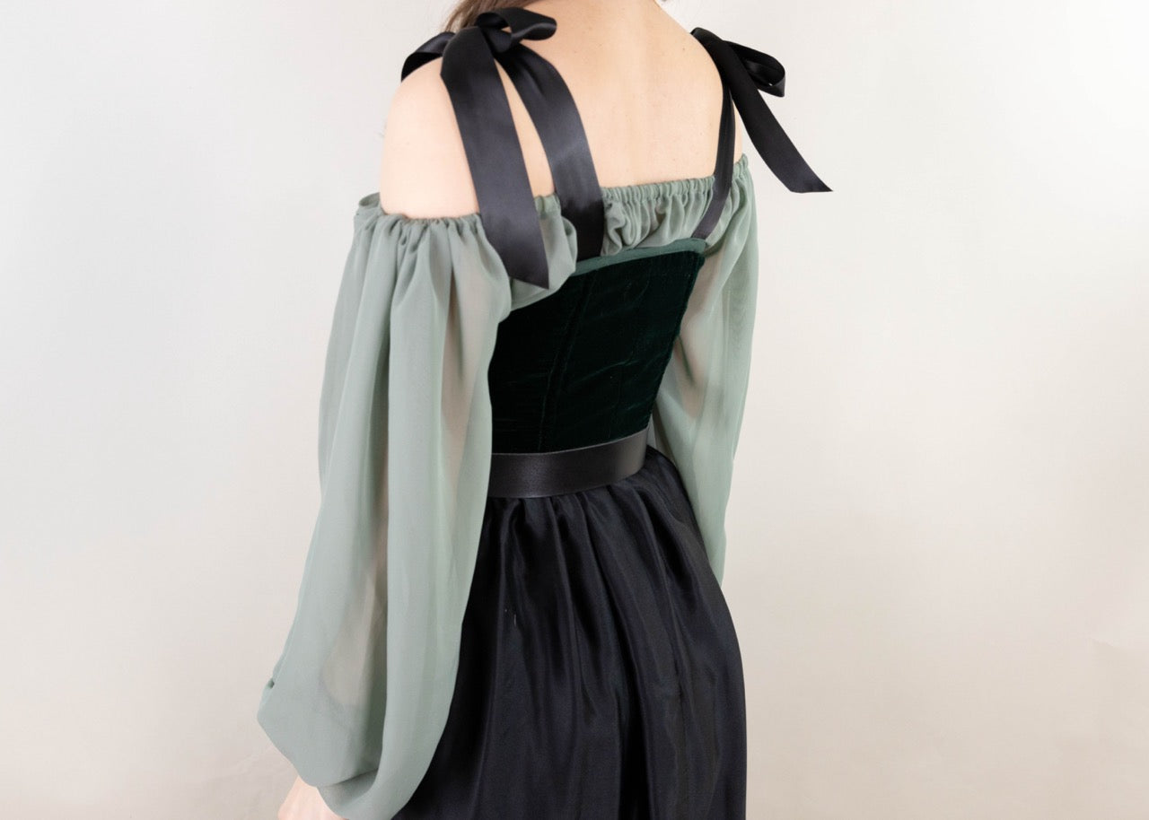 Back view of a woman wearing a Handmade Green Velvet Renaissance Corset with sheer green sleeves and black skirt