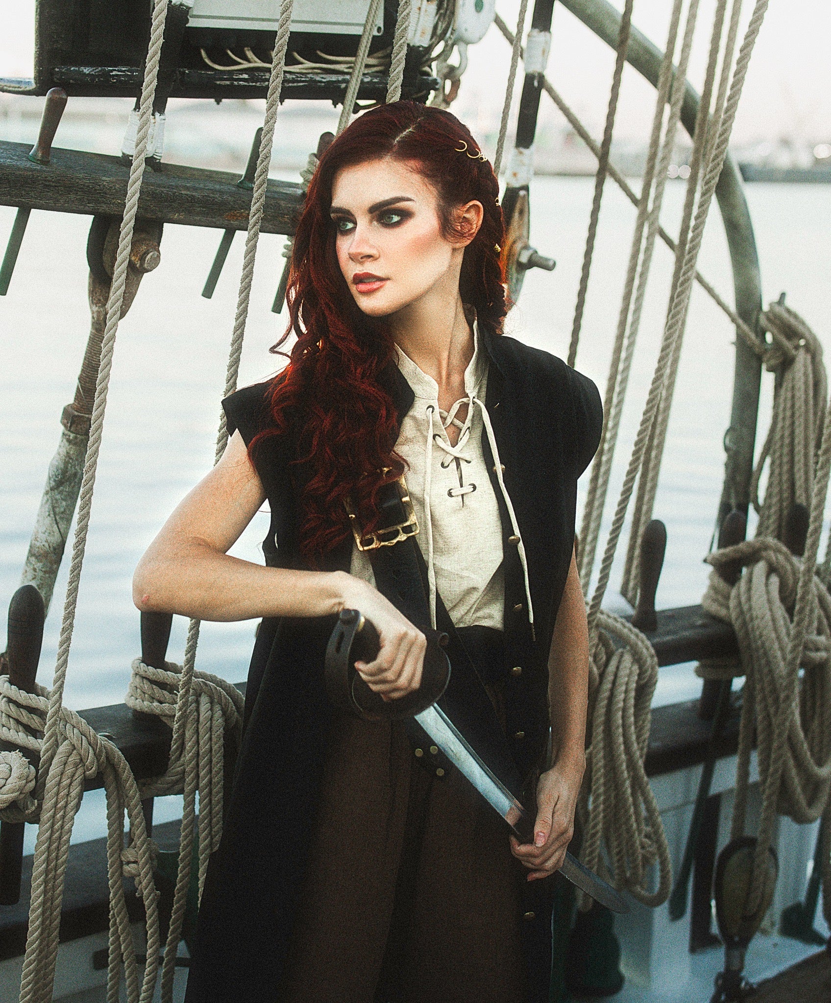 Woman wearing Linen Sleeveless Pirate Tank with lace-up neckline posing on a ship holding a sword confidently