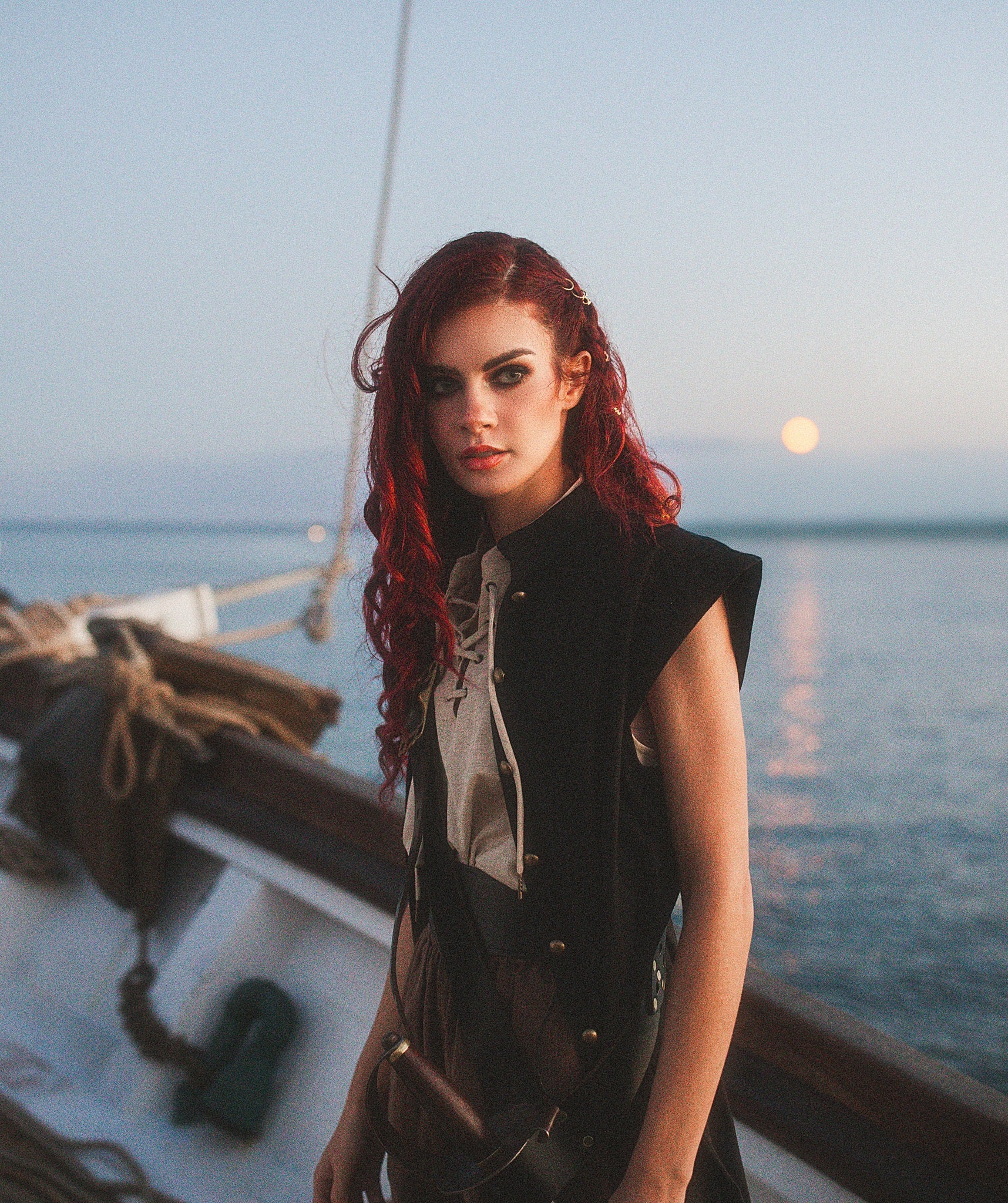 Woman with red hair wearing Linen Sleeveless Pirate Tank standing on a boat by the ocean at sunset