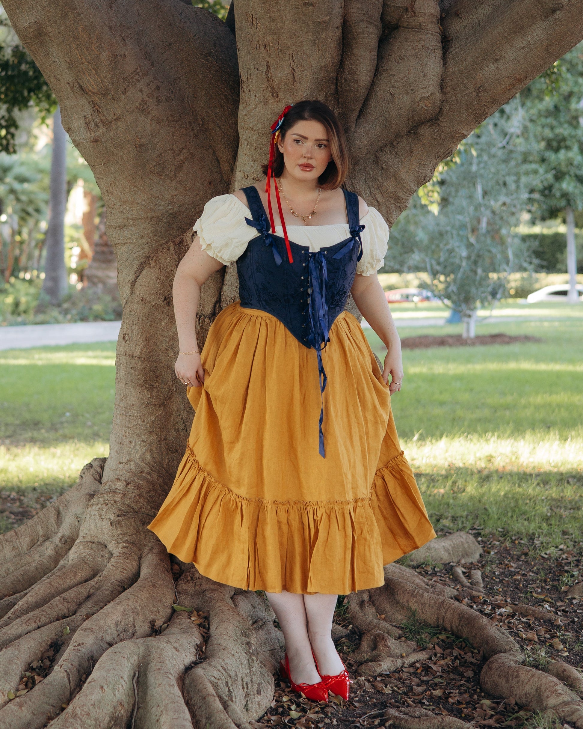 Woman standing by tree wearing Yellow Linen Ruffle Skirt paired with navy corset and white puff sleeve top outdoors