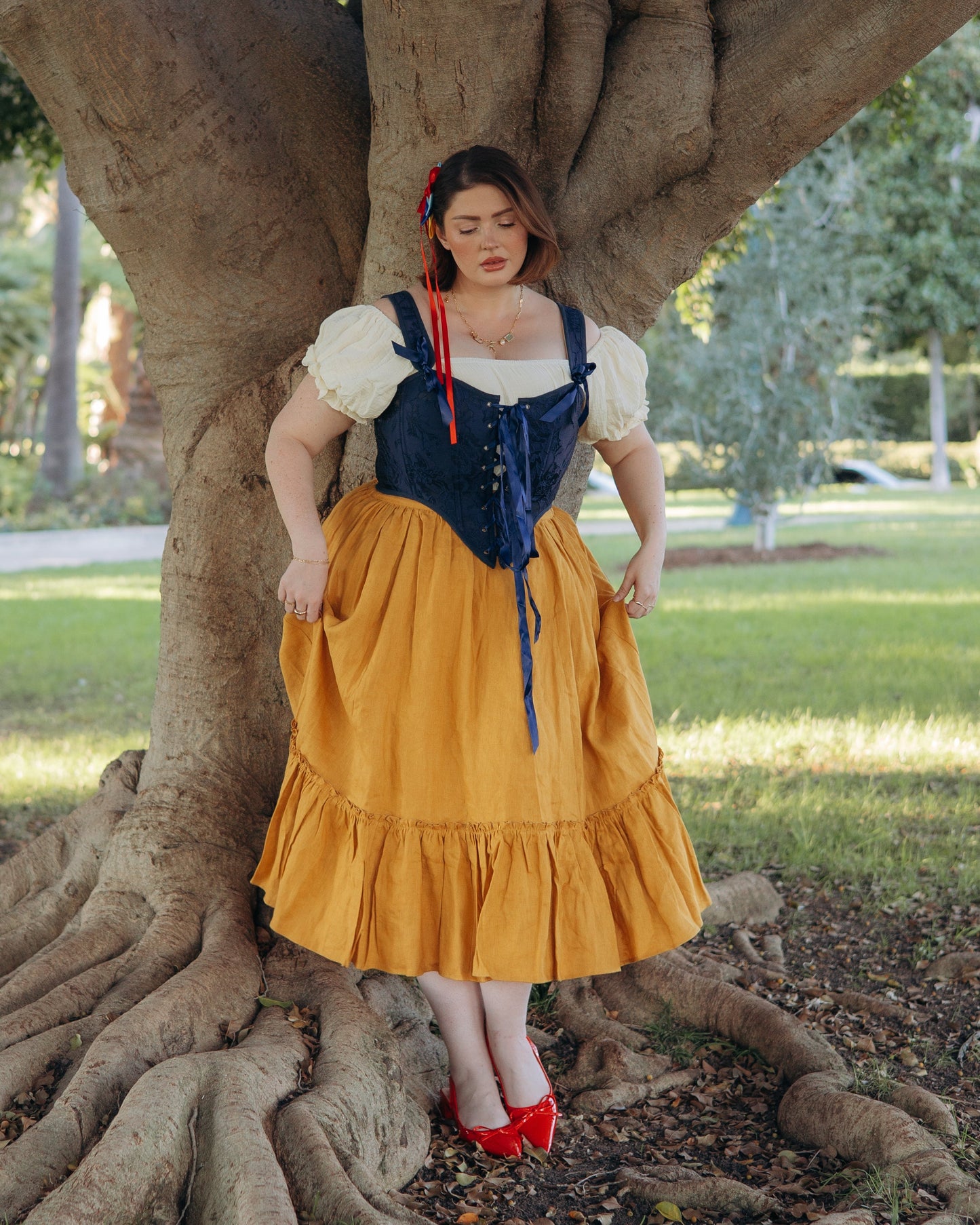 Woman wearing a dark blue floral jacquard corset standing against a large tree in a park setting
