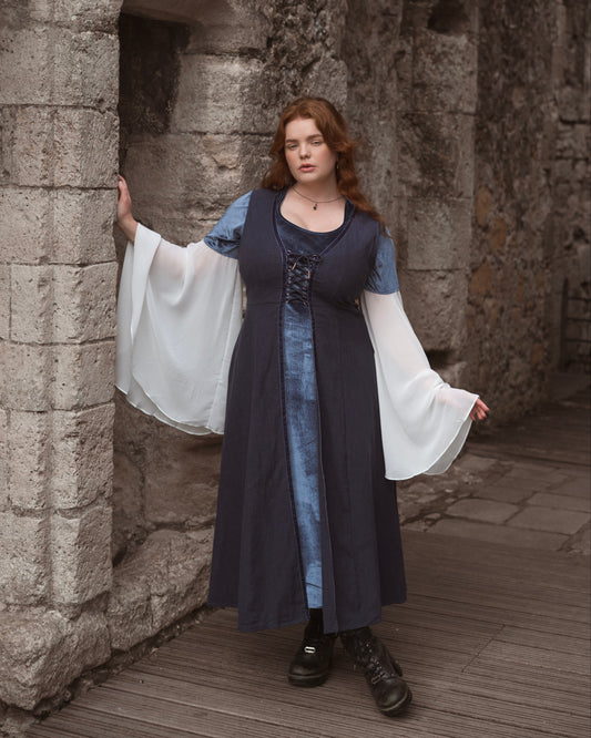 Woman wearing Elven Blue Velvet Bell Sleeve Dress with sheer white chiffon sleeves posing by stone wall outdoors