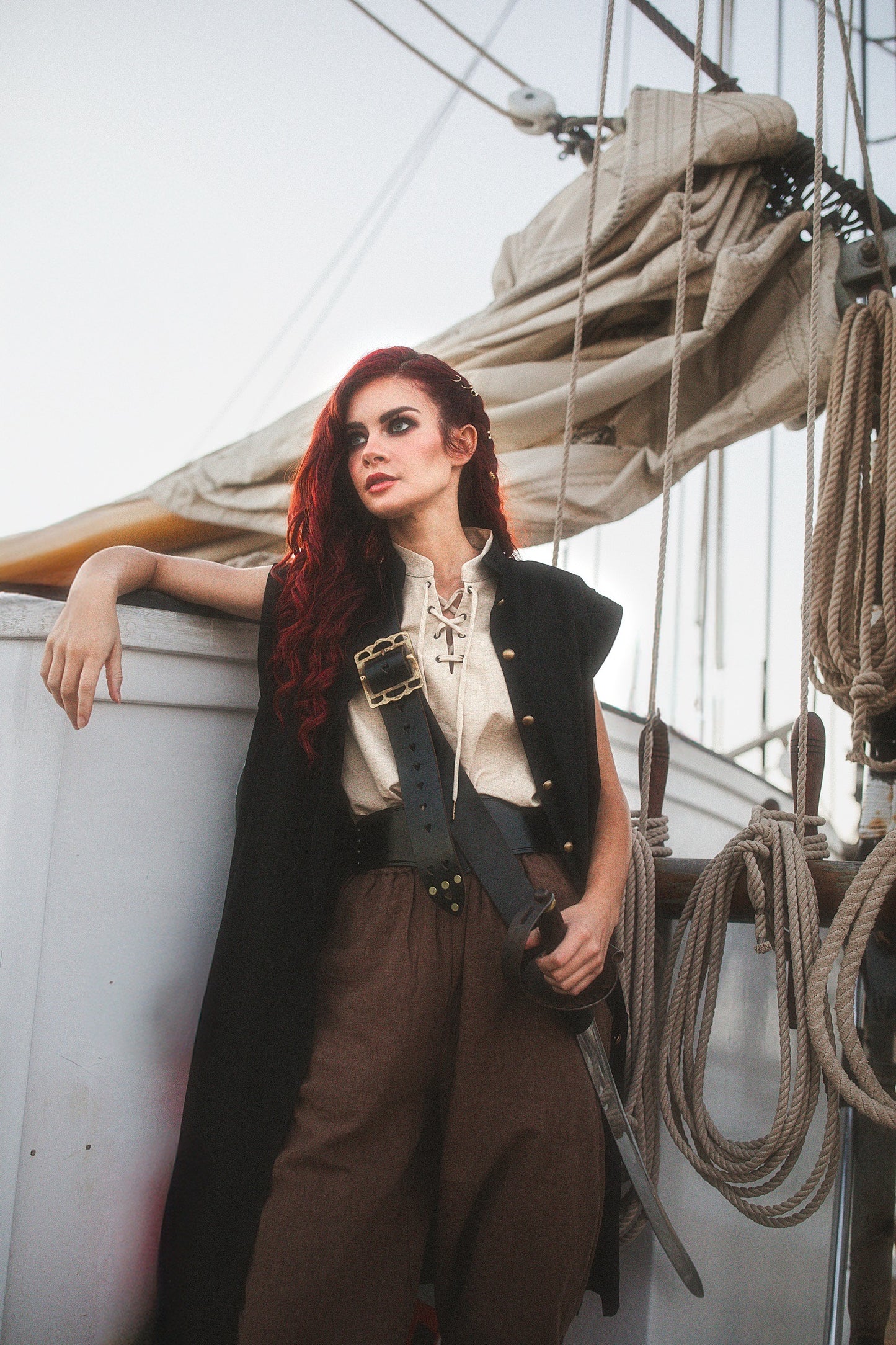 Woman wearing a Linen Sleeveless Pirate Tank with lace-up neckline standing on a ship deck with sails and ropes behind her
