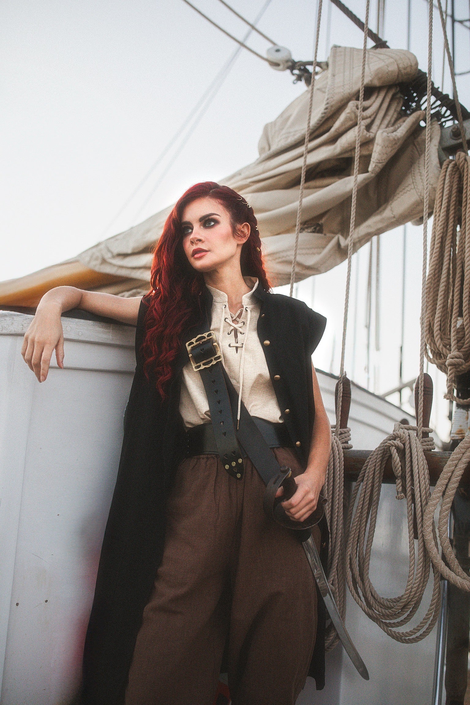 Woman wearing a Linen Sleeveless Pirate Tank with lace-up neckline standing on a ship deck with sails and ropes behind her