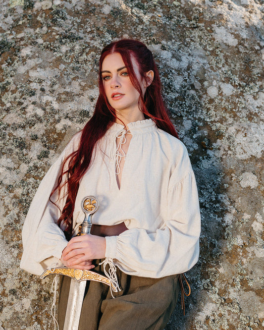 Woman wearing a Borgia Shirt inspired by Italian Renaissance linen chemises holding an ornate sword against a rocky background