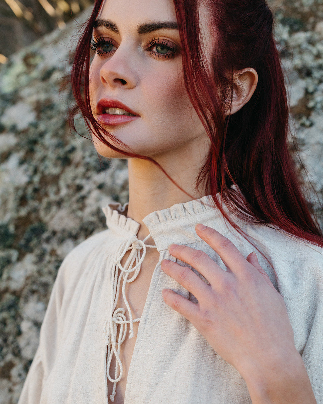 Close-up of a woman wearing the Borgia Shirt with a delicate tie neckline and textured natural fabric outdoors