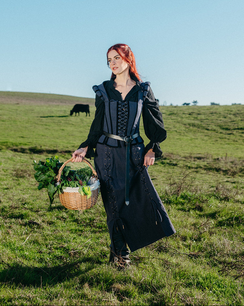 Woman wearing a black Tavern Skirt with lace-up details standing in a grassy field holding a basket of greens