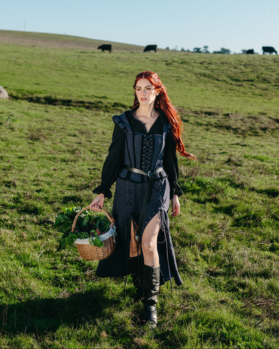 Woman wearing Navy Tavern Bodice dress walking in a green field carrying a basket of greens under bright sunlight