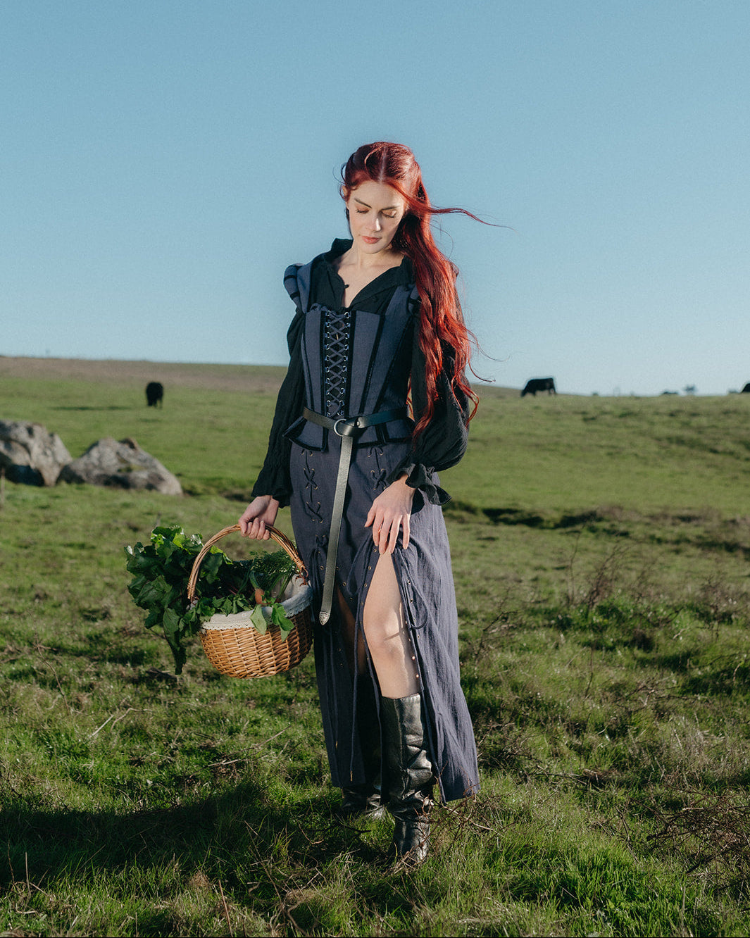 Woman in a field wearing a Navy Tavern Bodice with long skirt and boots holding a basket of greens under a clear sky