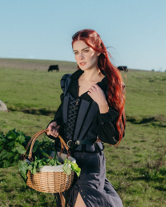 Woman wearing Navy Tavern Bodice holding a basket of greens in a green field with distant cows