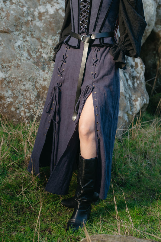 Woman outdoors wearing a dark blue Tavern Skirt with laced details and black boots beside a rock wall