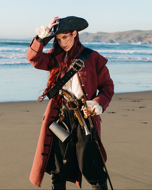 Woman standing on beach wearing a red Pirate Captain's Coat with black trimmings and pirate accessories