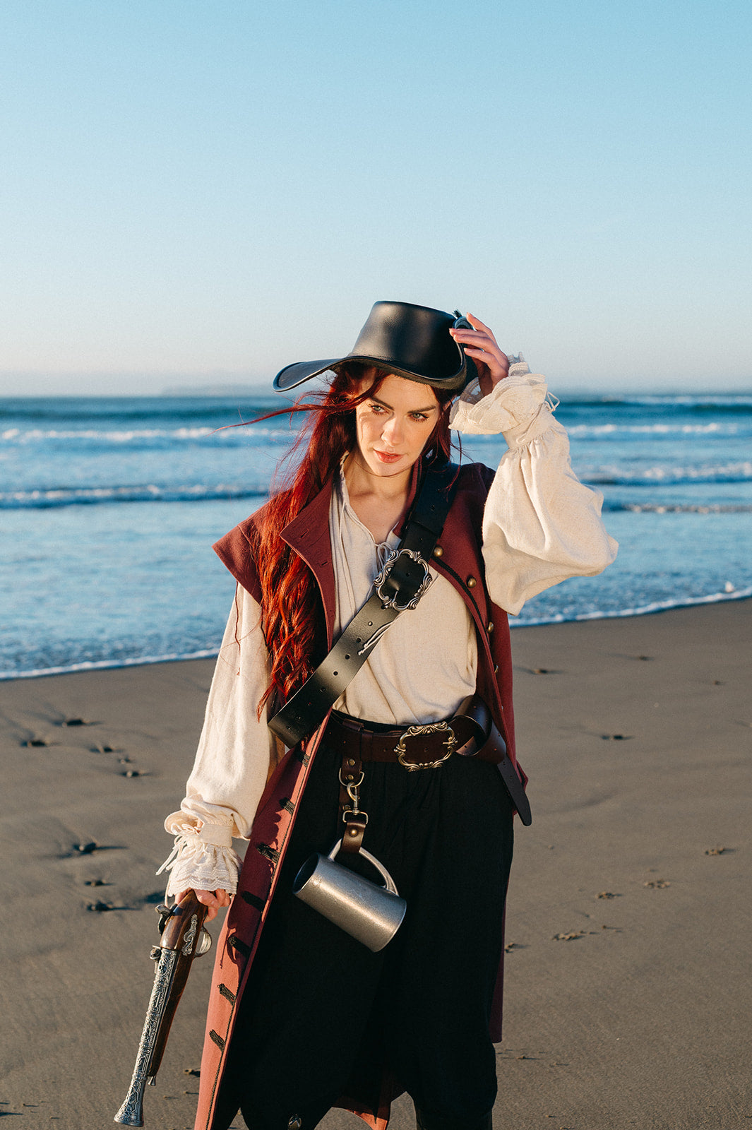 Woman wearing Borgia Shirt with flowing sleeves standing on beach holding a pistol under clear sky