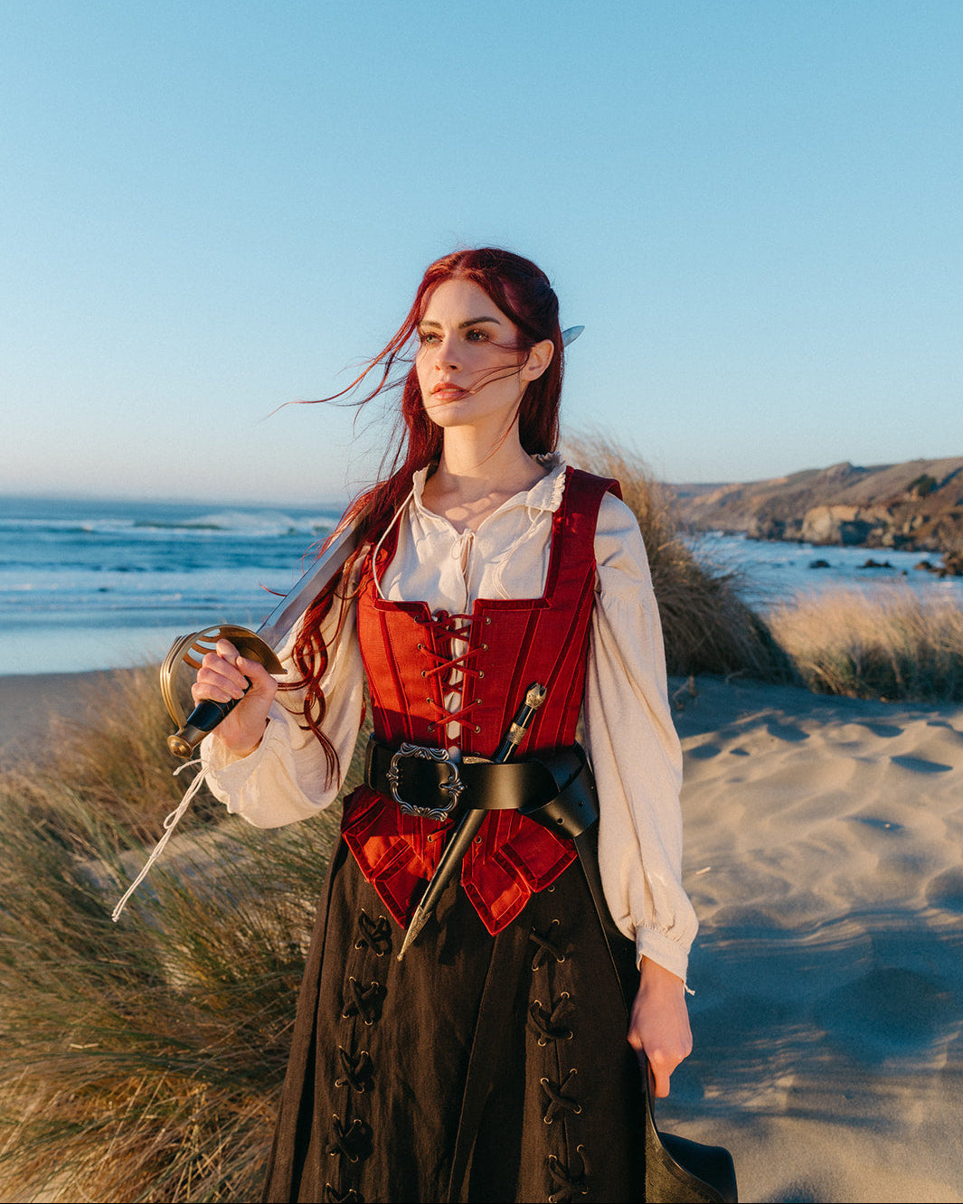 Woman on beach dressed as pirate wearing a Leather Pirate Belt holding a sword with wind in her hair