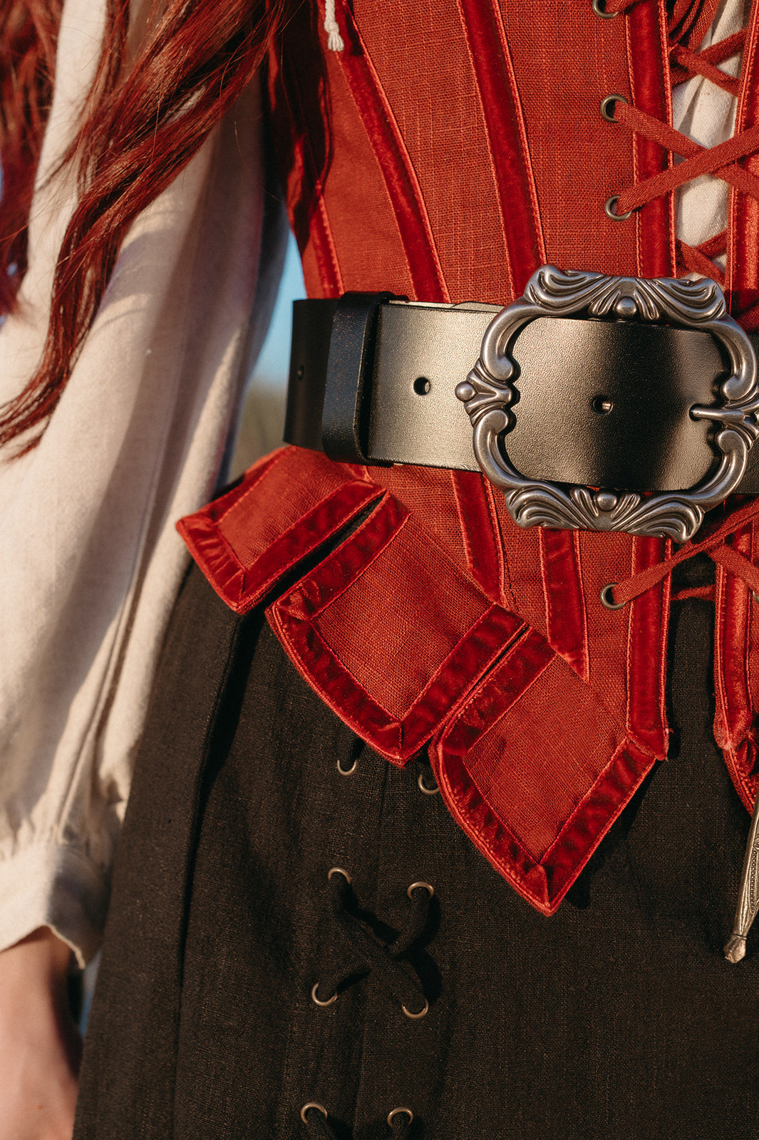 Close-up of a Leather Pirate Belt with ornate buckle worn over a red corset and dark skirt in warm light