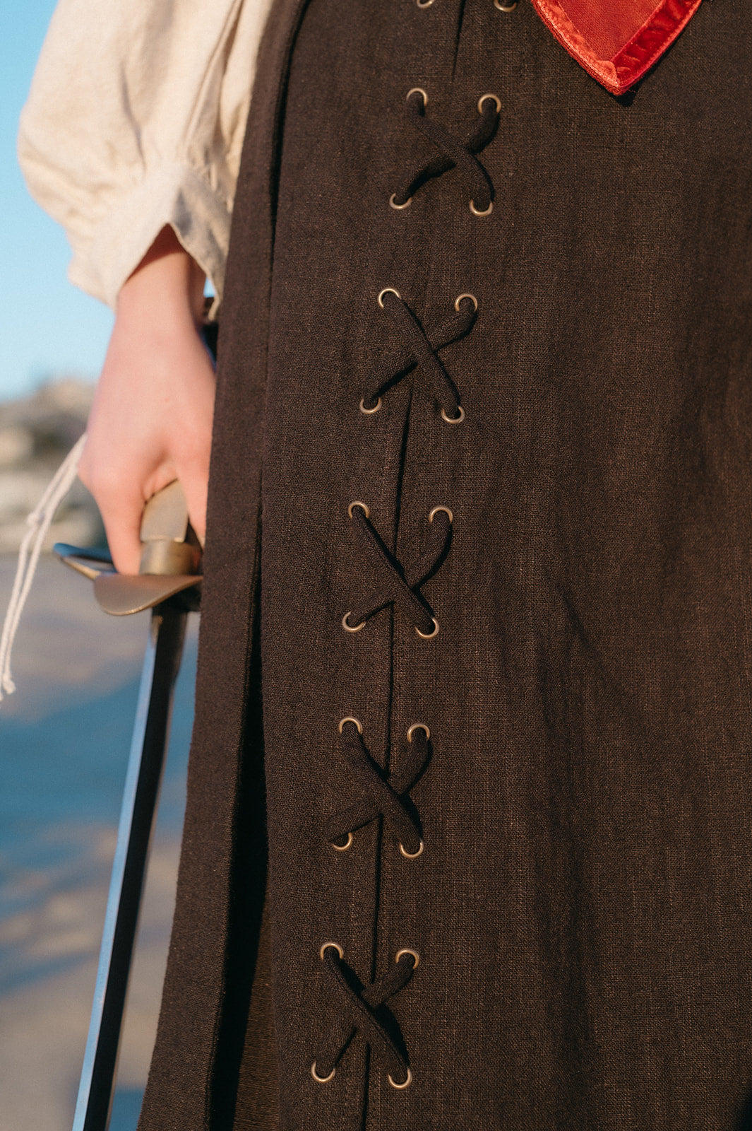 Close-up of black Tavern Skirt with lace-up detail worn with medieval-style blouse and sword held at side