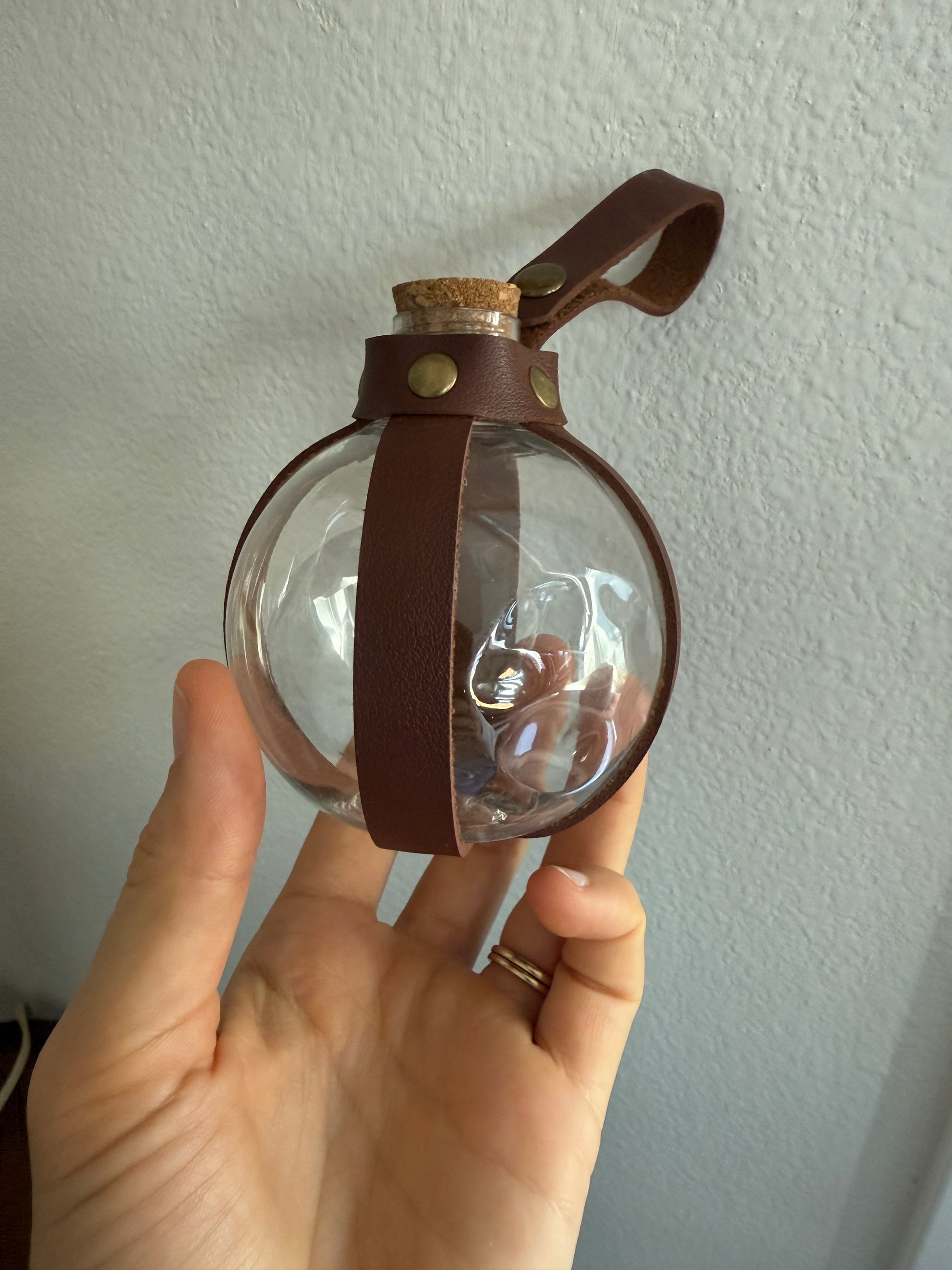 Potion Bottle -- slightly damaged *Final Sale* held in hand with visible dent and leather strap detail against a plain background
