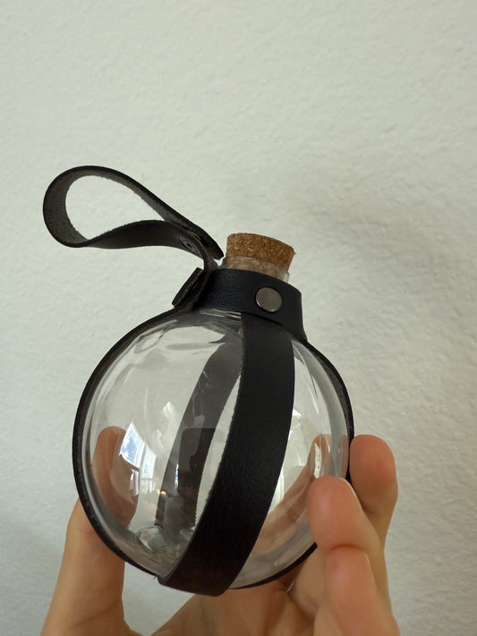 Hand holding Potion Bottle -- slightly damaged *Final Sale* with cork top and black leather strap showing minor dents on plastic.
