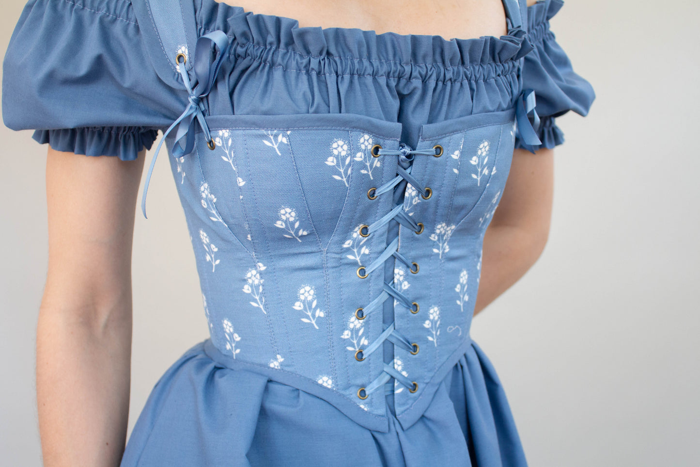 Woman wearing Handmade Blue and White Floral Regency Stays - Size XS with lace-up front and puff sleeves in soft blue fabric