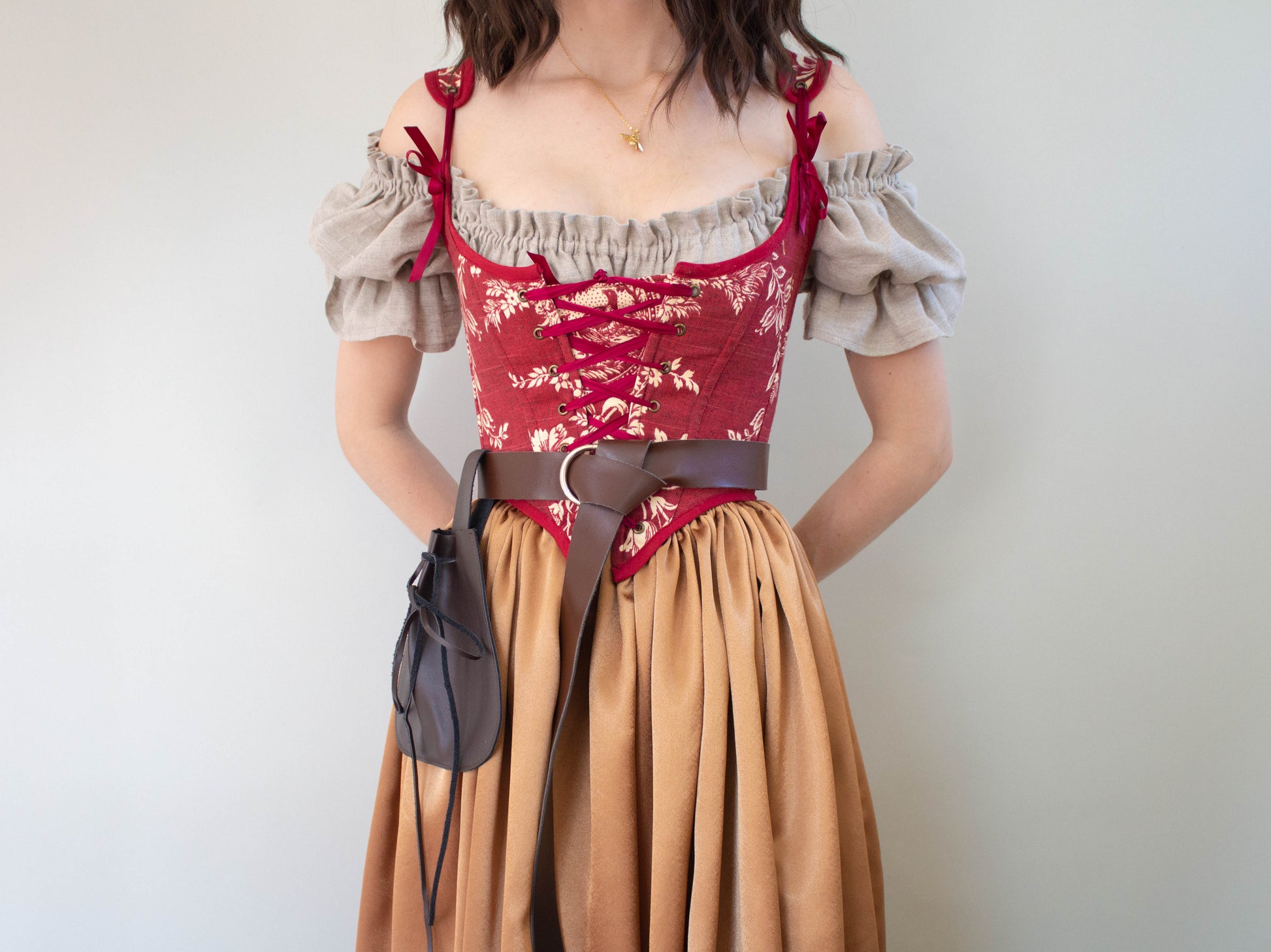 Woman wearing a Handmade Dark Red Toile Corset with beige off-shoulder blouse and tan skirt, styled with brown belt and bag