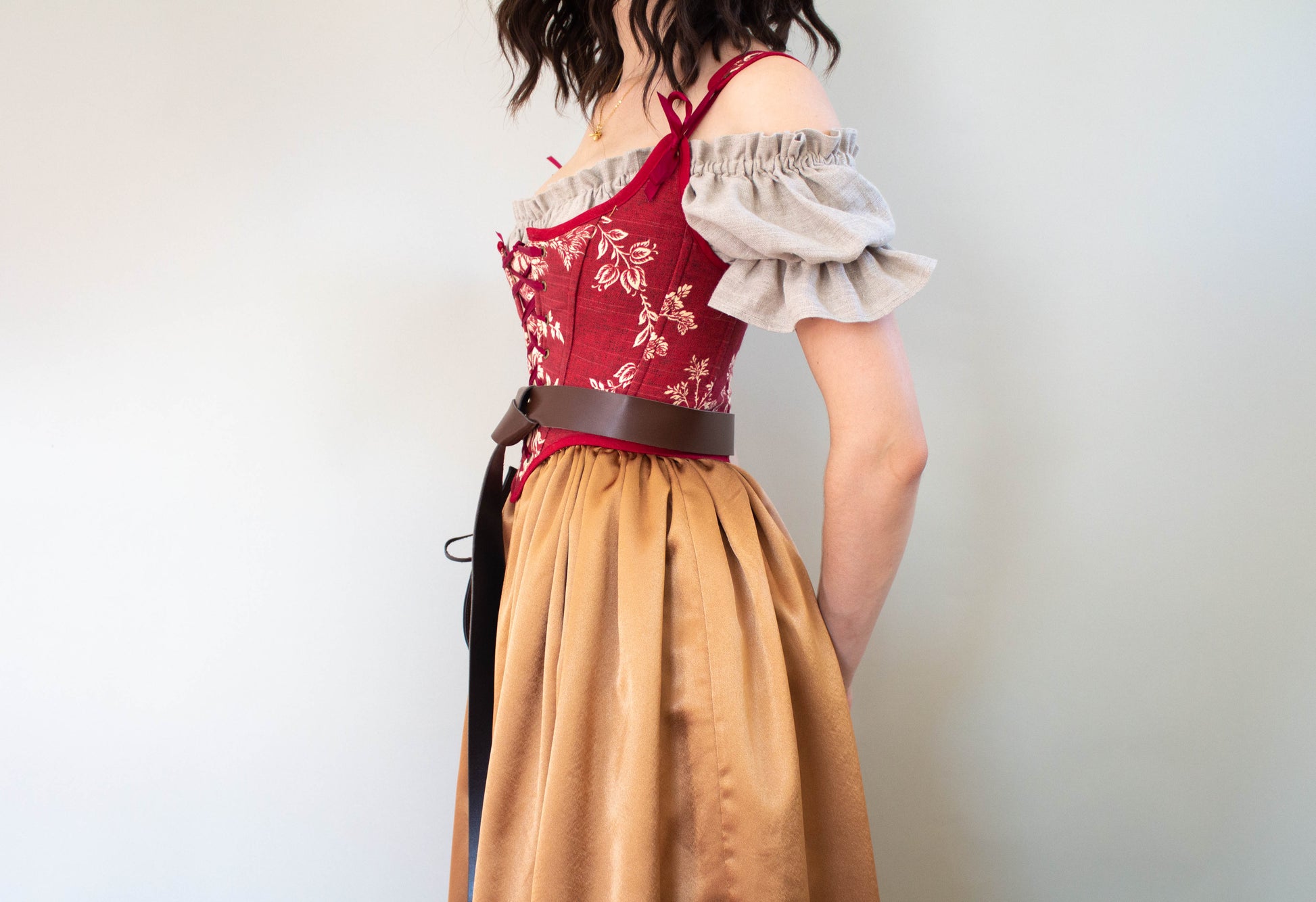 Woman wearing a Handmade Dark Red Toile Corset with floral pattern and puffed beige blouse against a plain background