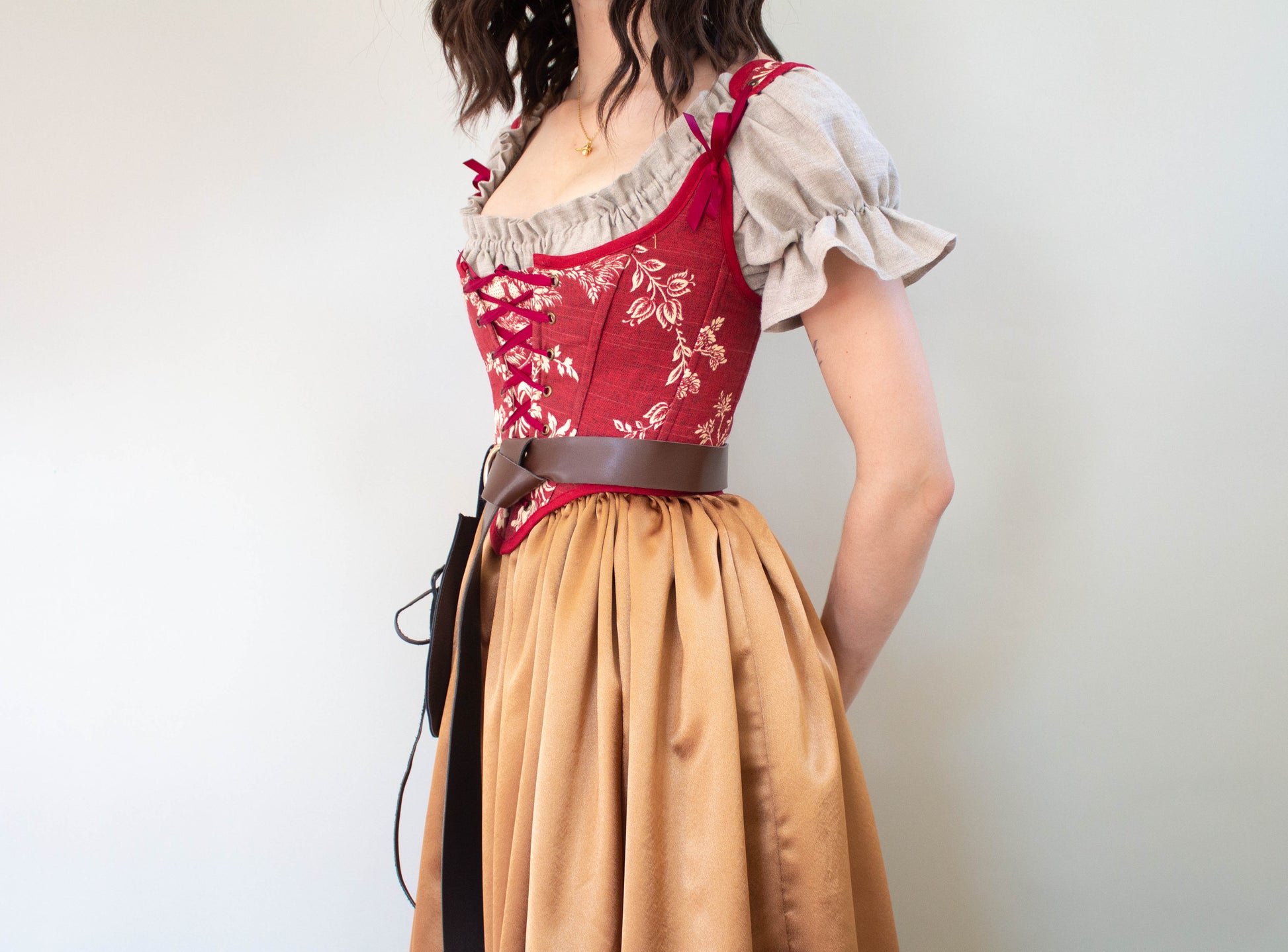 Woman wearing a Handmade Dark Red Toile Corset with floral pattern and beige puff sleeve blouse standing sideways
