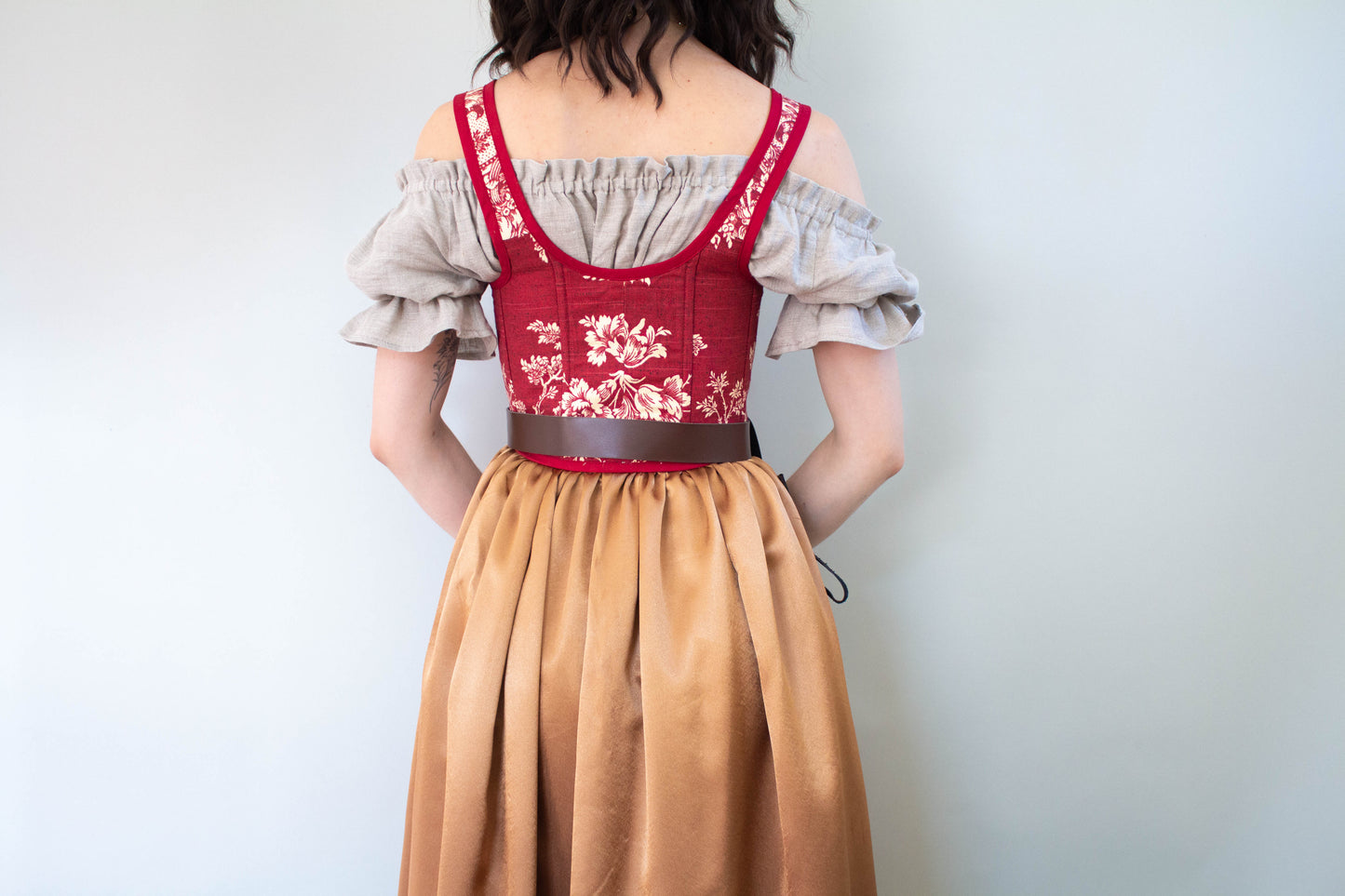 Back view of a woman wearing a Handmade Dark Red Toile Corset with floral patterns and a beige skirt