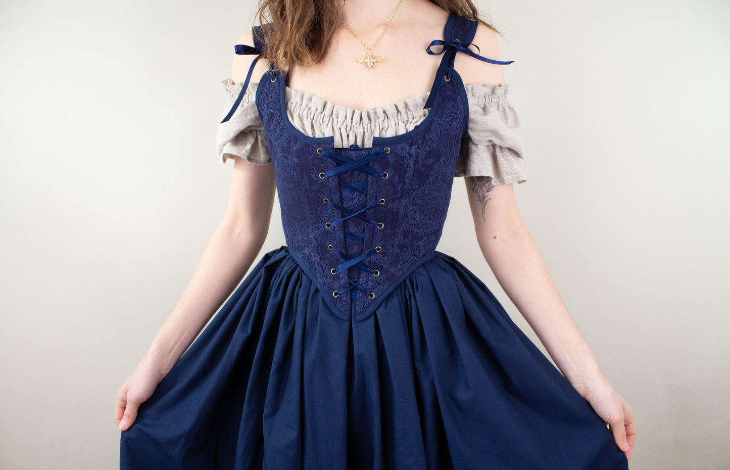 Woman wearing a Handmade Navy Blue Embroidered Floral Corset over an off-shoulder beige blouse holding skirt sides.