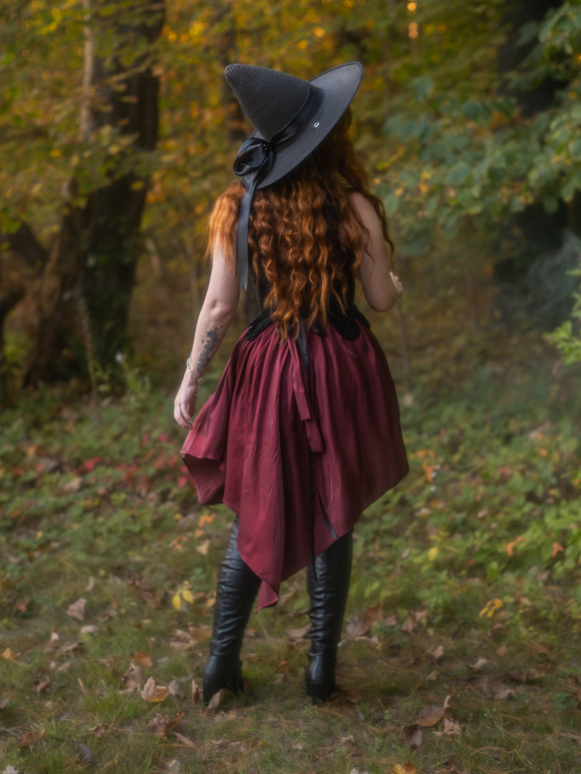 Woman wearing Dark Red Flutter Dress with handkerchief hem and black boots standing in autumn forest