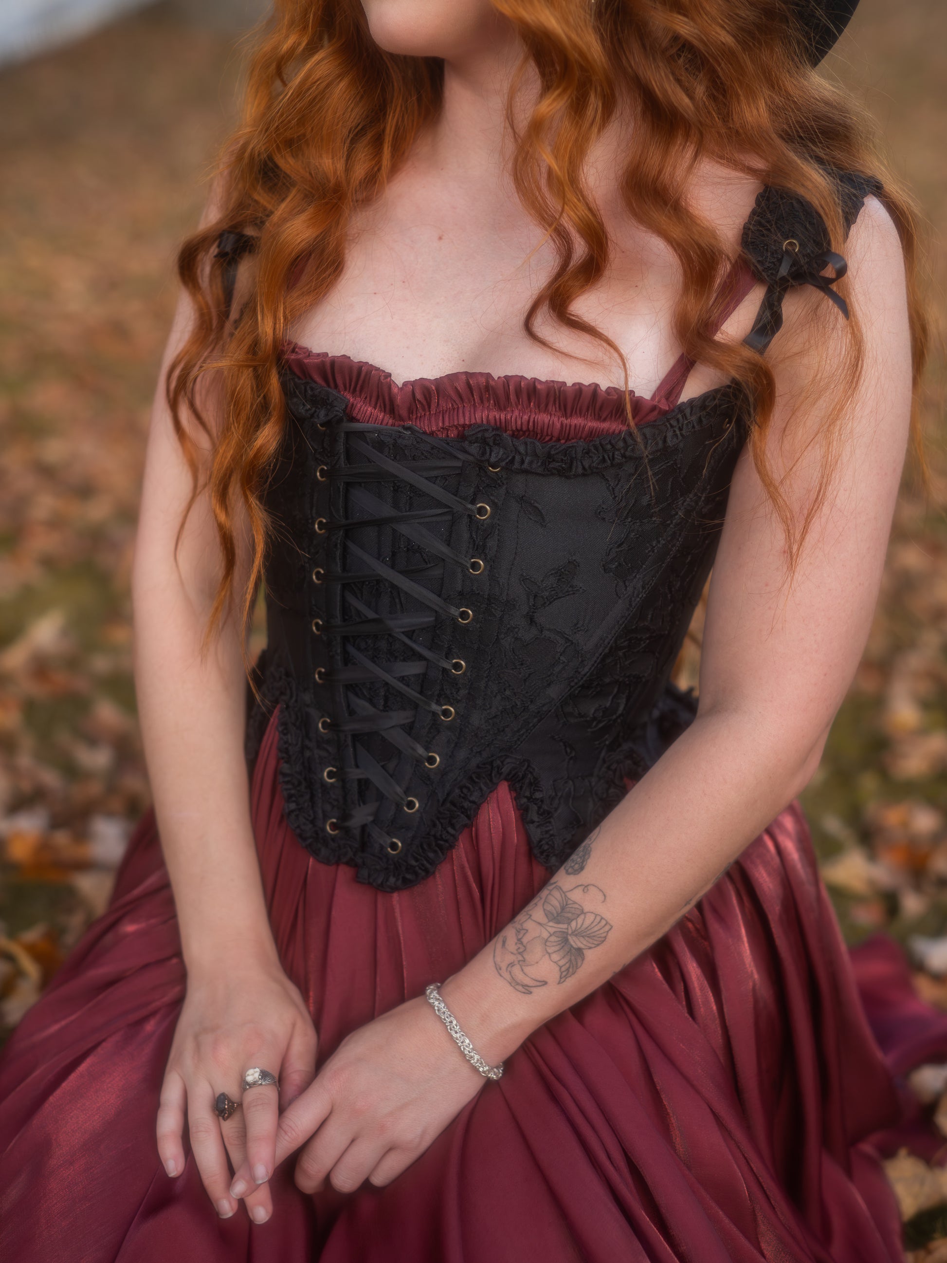 Woman wearing a Dark Red Flutter Dress with lace-up black corset detail sitting outdoors on autumn leaves