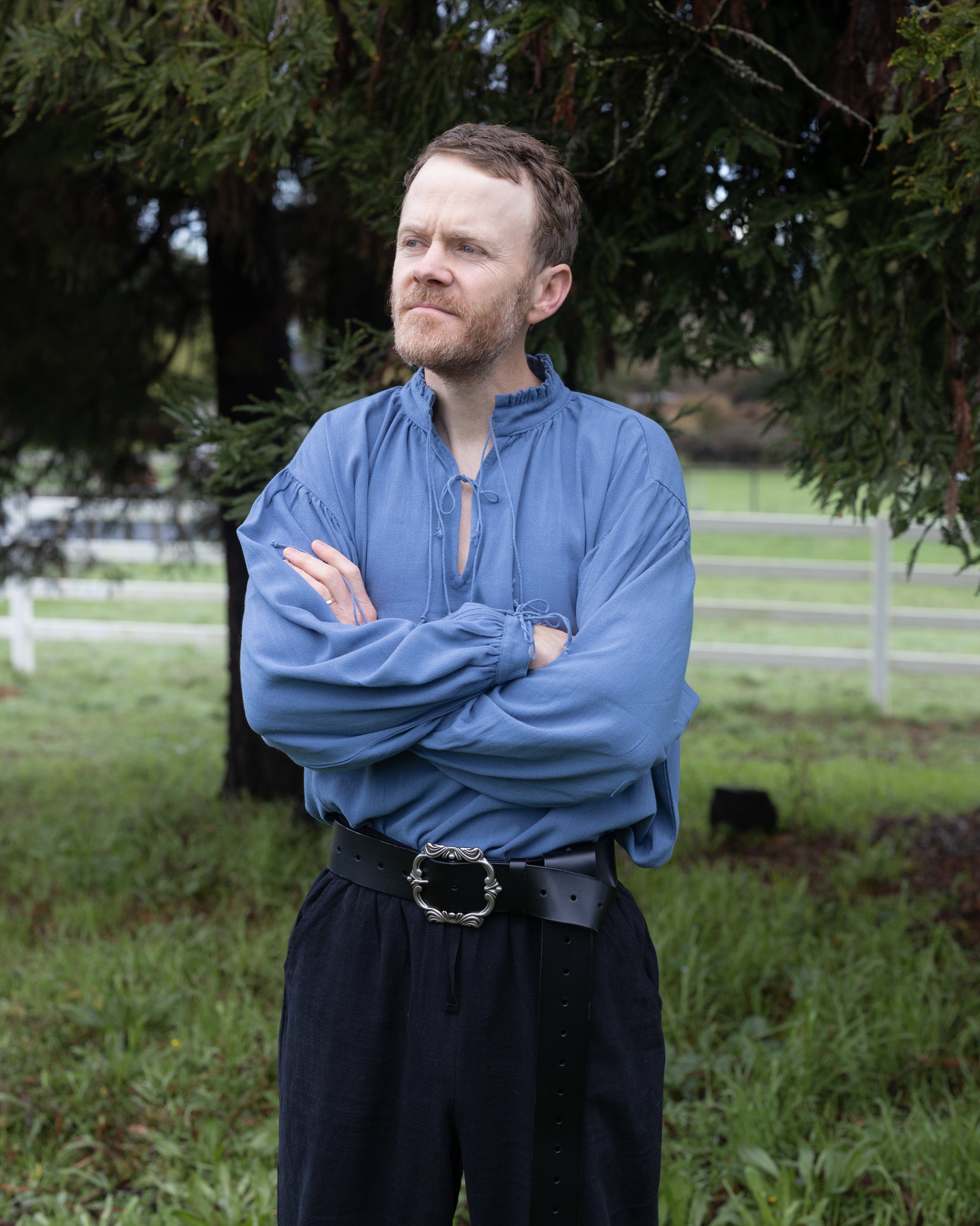 Man wearing blue Borgia Shirt with gathered cuffs and neckline standing outdoors with arms crossed