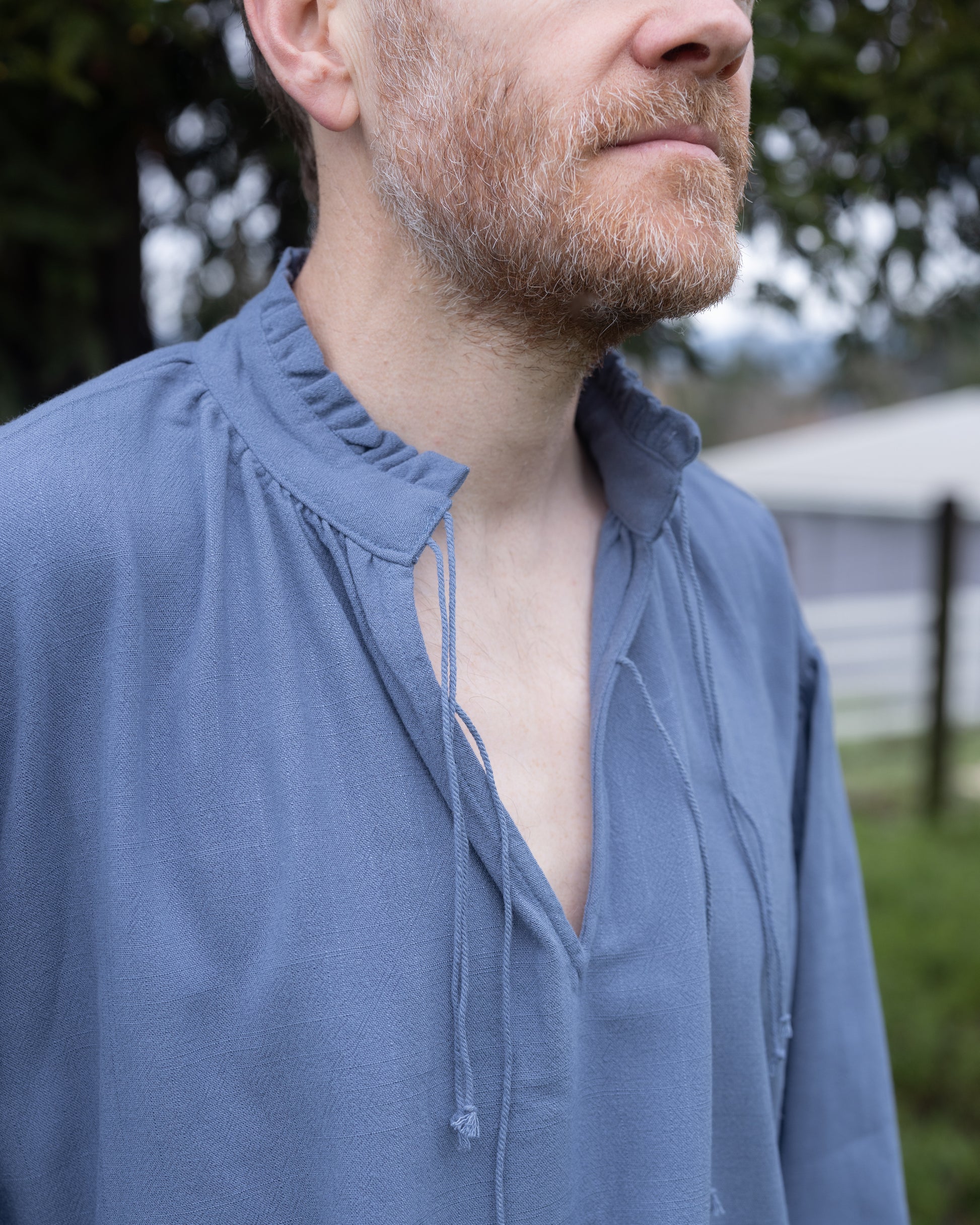 Close-up of man wearing a soft linen Borgia Shirt with a ruffled collar and open neckline outdoors