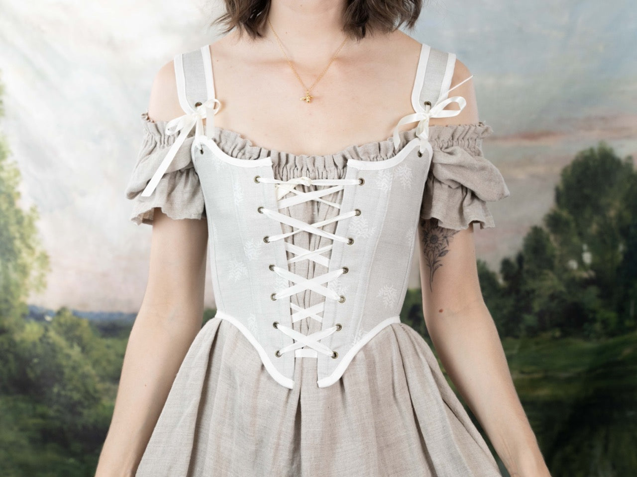 Woman wearing a Handmade Beige Fern Corset over an off-shoulder linen dress with a laced front and bow details.
