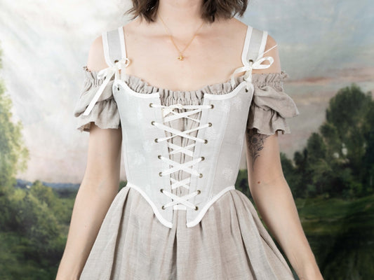 Woman wearing a Handmade Beige Fern Corset over an off-shoulder linen dress with a laced front and bow details.
