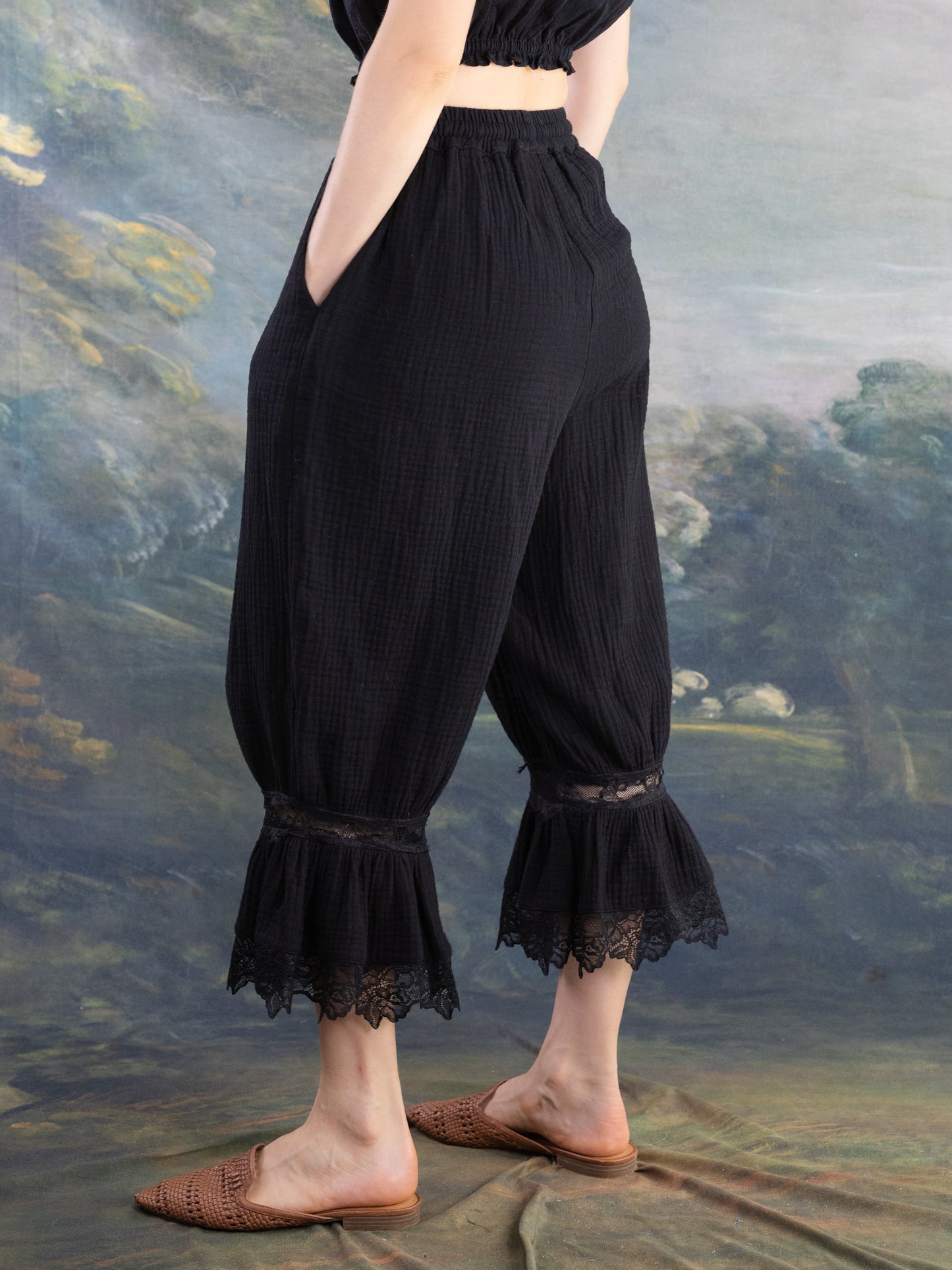 Woman wearing black Bloomer Pantaloons with lace trim standing against a painted backdrop in relaxed pose