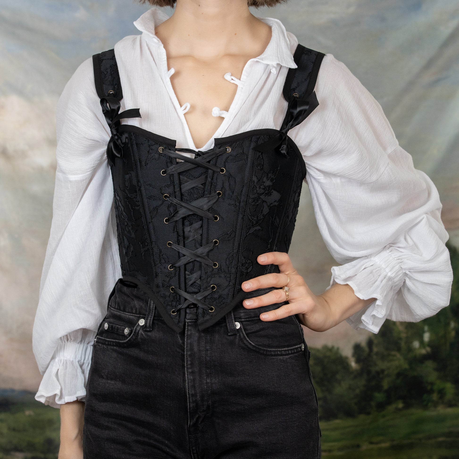 model wearing a black pirate corset with black pants and a white long sleeve poet blouse