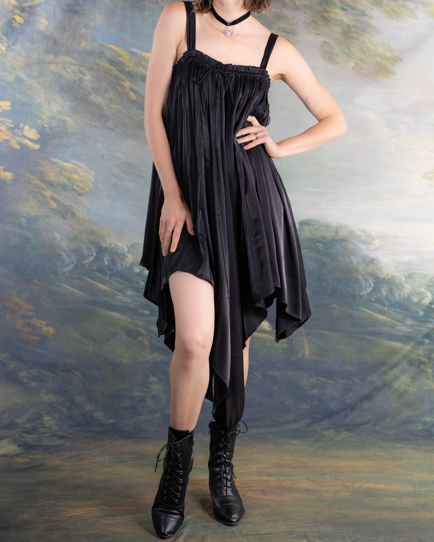 Woman wearing Black Flutter Fairy Dress with handkerchief hem and satin fabric paired with black boots