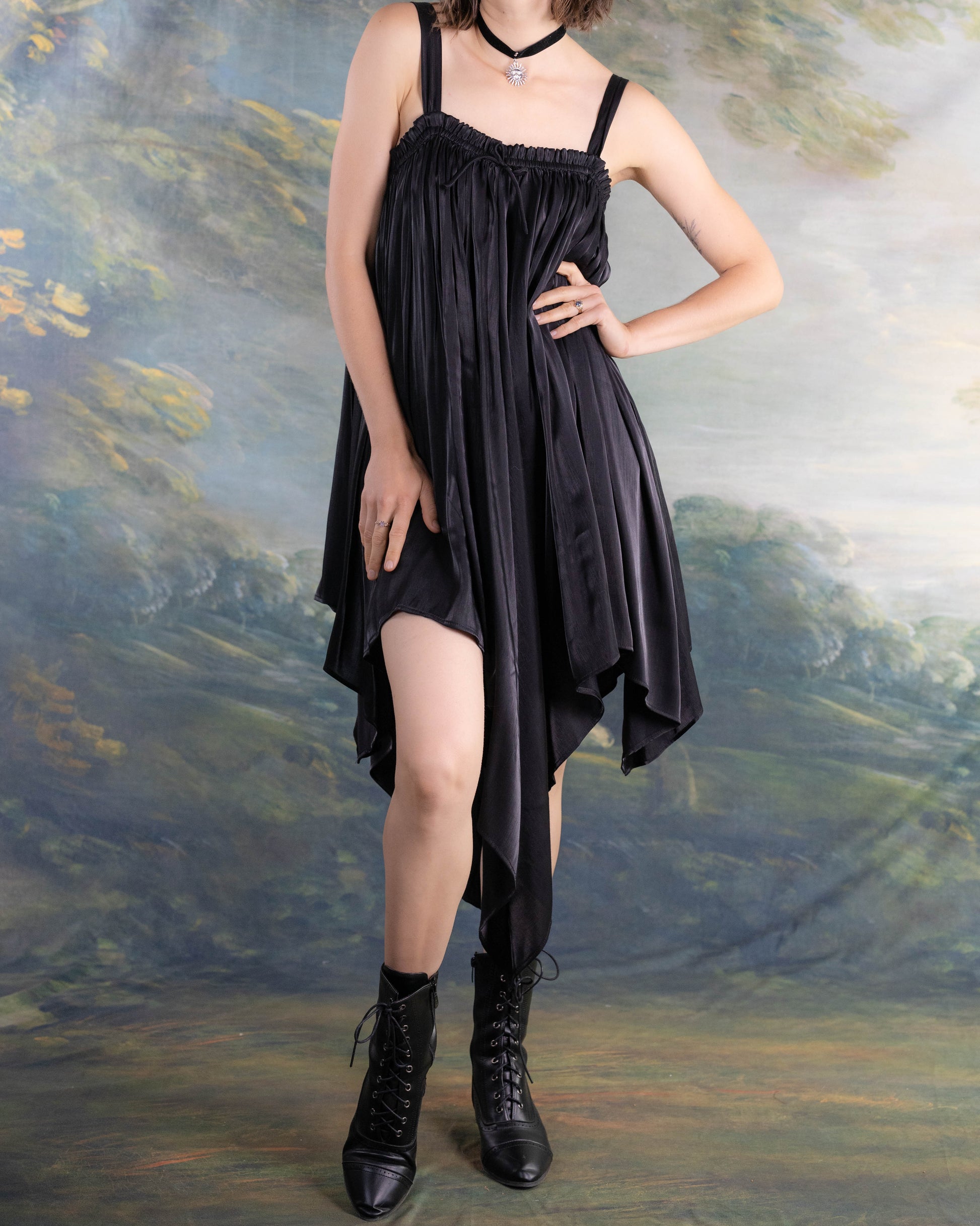 Woman wearing Black Flutter Fairy Dress with handkerchief hem and satin fabric paired with black boots