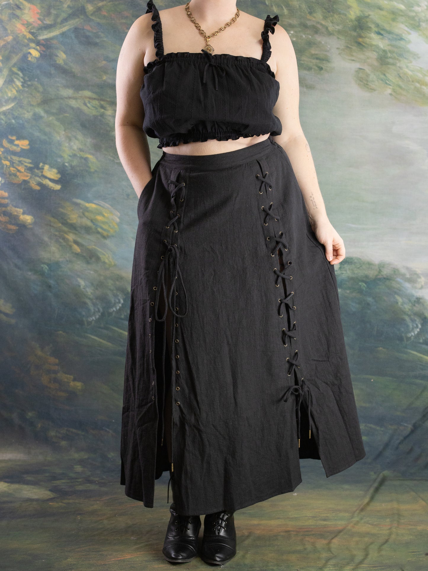 Woman wearing black Lacey Chemisette Tank styled with a long black lace-up skirt and black ankle boots in soft lighting