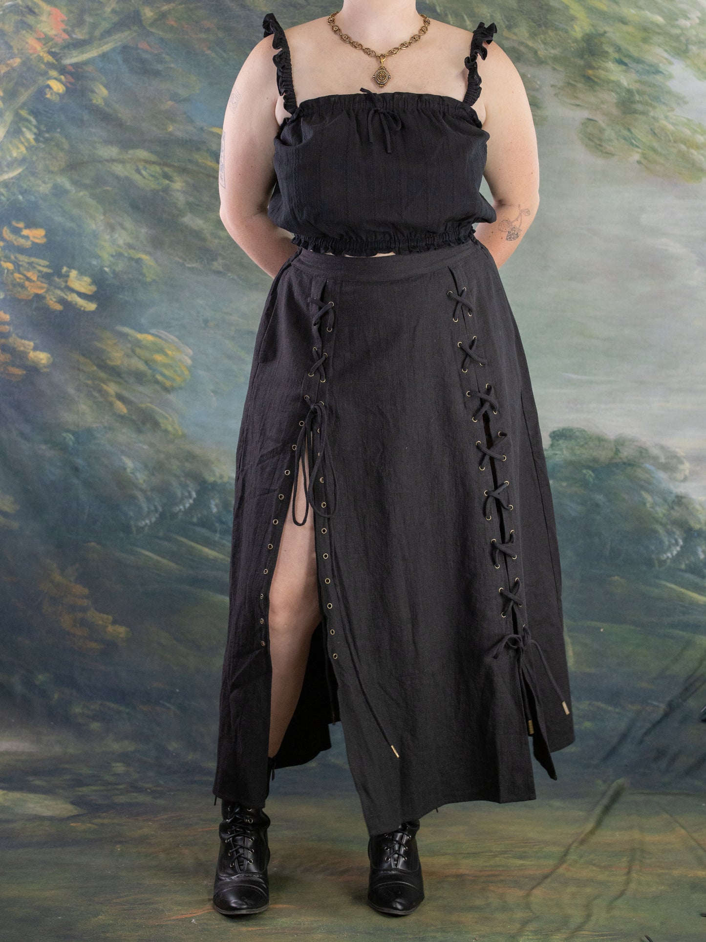 Front view of a model wearing a black Lacey Chemisette Tank with lace-up details and boots against a scenic backdrop