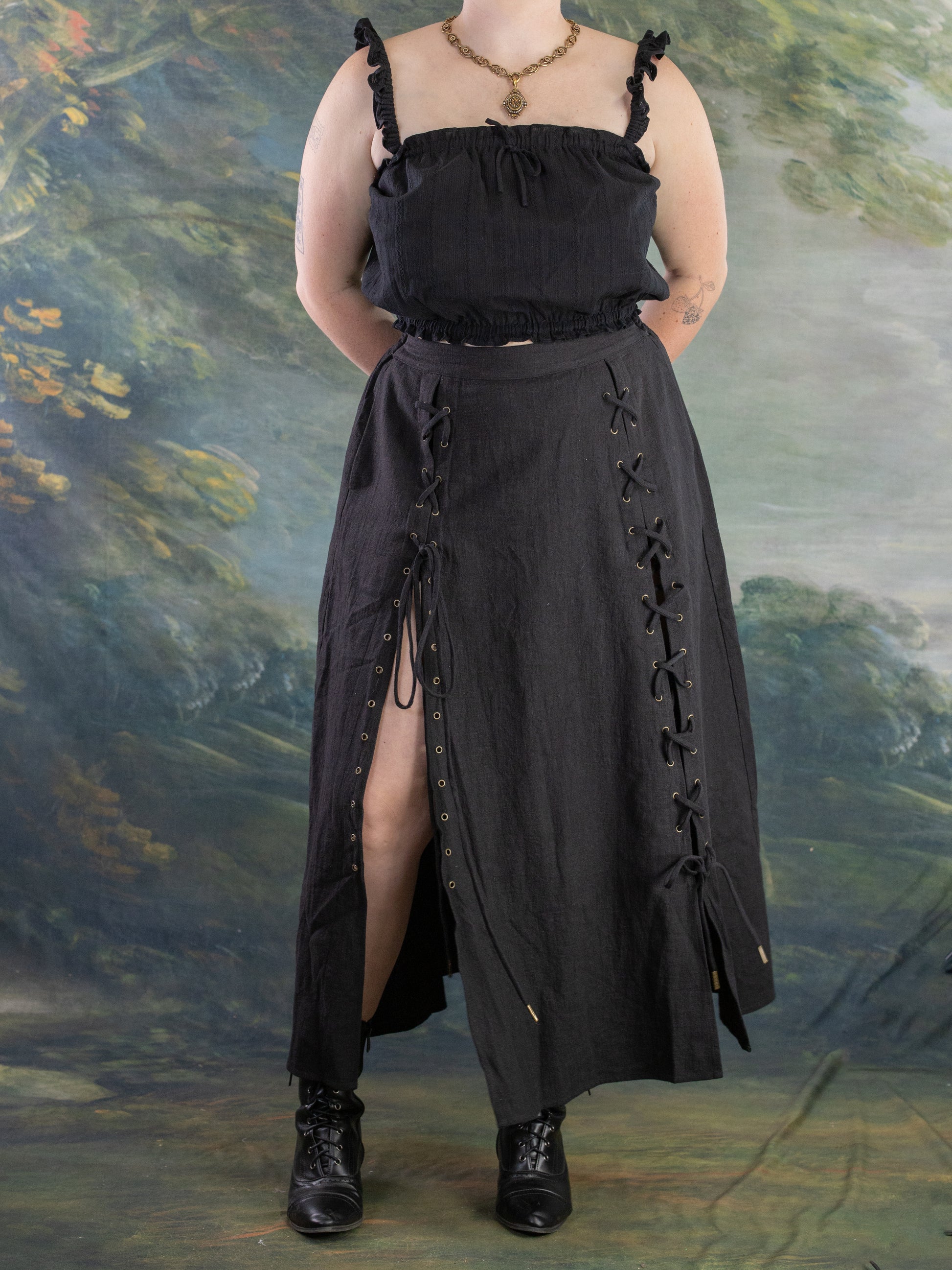 Front view of a model wearing a black Lacey Chemisette Tank with lace-up details and boots against a scenic backdrop