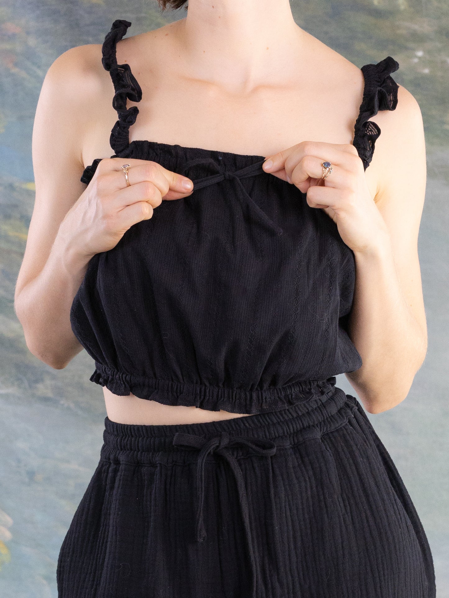 Close-up of hands adjusting the bow on a black Lacey Chemisette Tank with ruffled shoulder straps and gathered hem