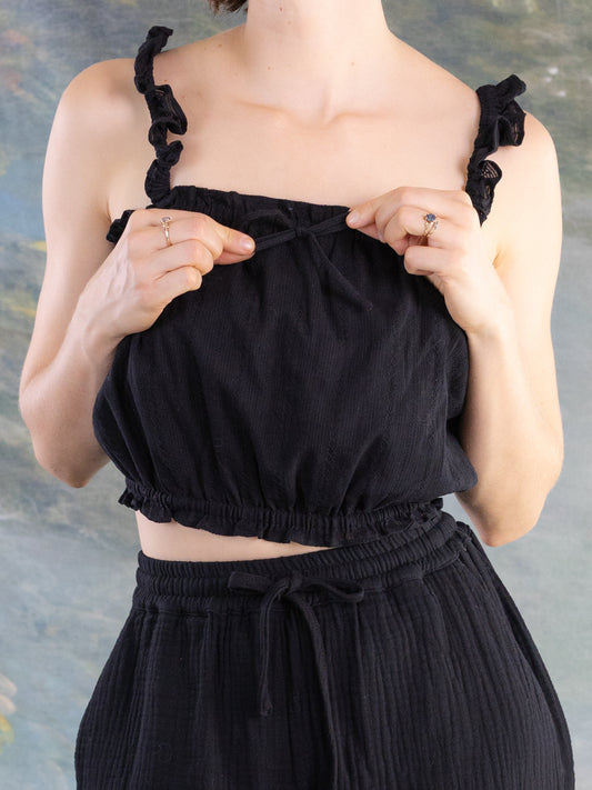 Close-up of hands adjusting the bow on a black Lacey Chemisette Tank with ruffled shoulder straps and gathered hem